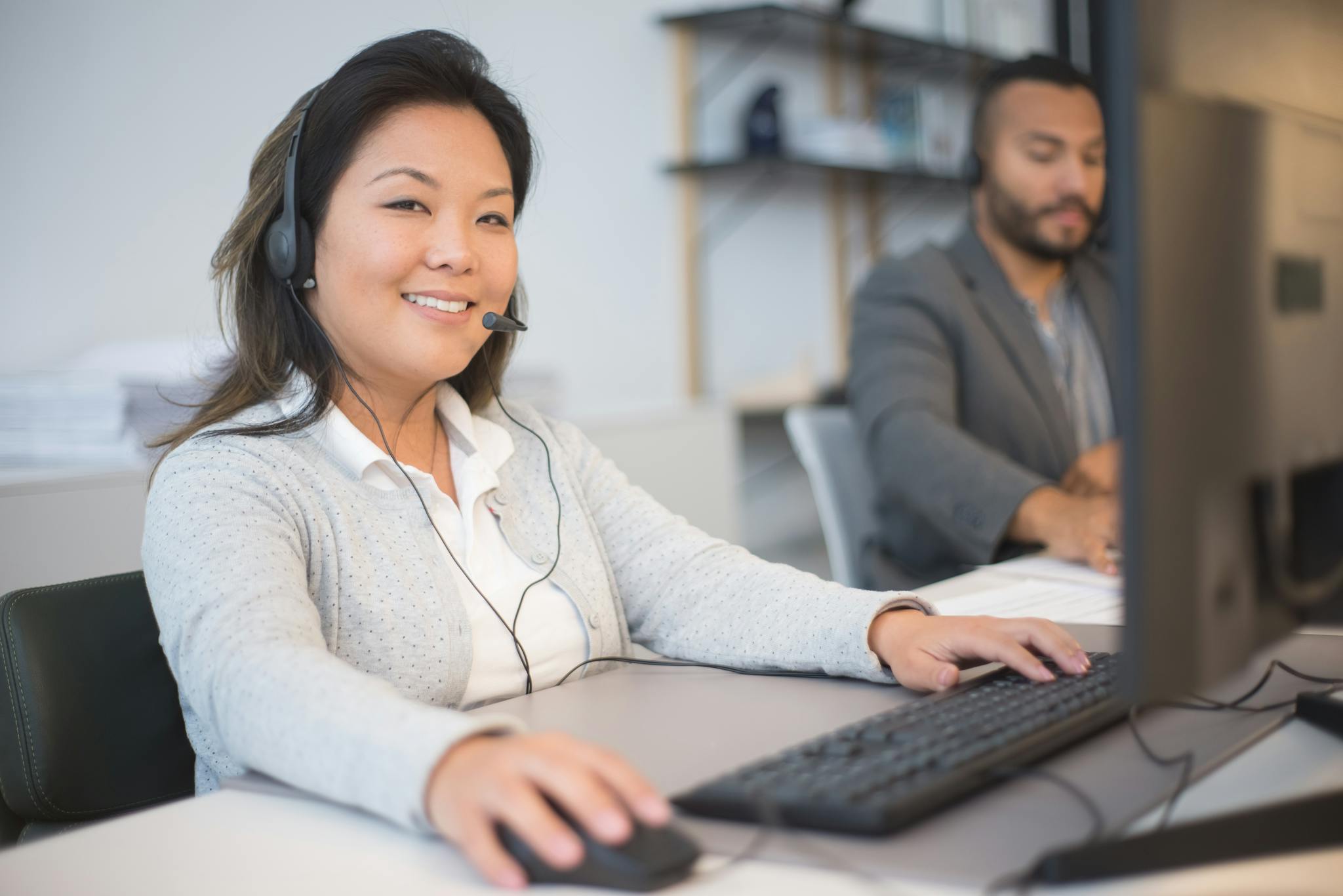 Two call center employees working with headsets in a modern office setting.